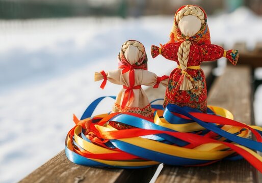 Two traditional maslenitsa dolls are placed on a pile of colorful ribbons on a wooden bench, celebrating the coming of spring