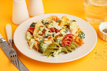 Delicious fusilli pasta with broccoli and cheese in plate on orange background, closeup