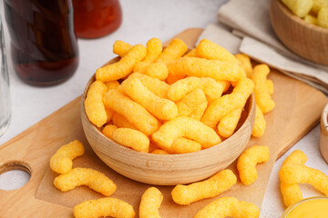 Wooden bowl with tasty salty corn sticks on light background, closeup