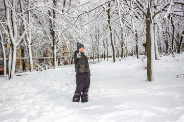 Naklejka premium eight-year-old boy standing in the snow, smiling, red cheeks, gloves covered with snow, hat, trees, branches, icicle, frost, winter, fun, walk, rest, weekend