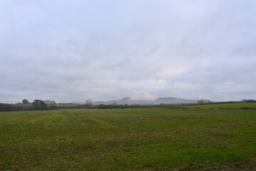 beautiful winter landscape with green field and hills in the distance and low lying clouds covering the landscape