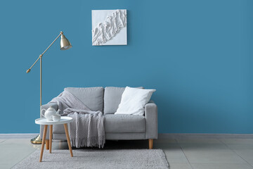 Stylish interior of blue living room with grey sofa, lamp and picture