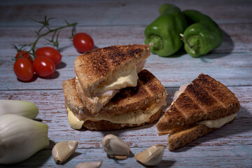 Toasted cheese and turkey sandwich on rustic table with cherry tomatoes, peppers, chives and garlic