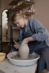 Blond woman shaping clay vase on pottery wheel working in studio