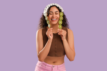 Beautiful young happy African-American woman holding sticks with kiwi on purple background