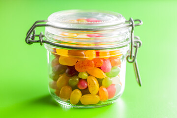 Multicolored jelly beans with various flavors in jar on green background.