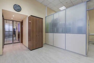 Spacious office hall with a brown wardrobe. Entrance glass door. A separate room in the .office, a wall of frosted glass.