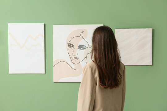 Young woman looking at paintings on green wall in art gallery, back view