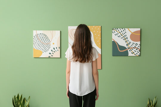 Young woman near paintings on green wall in art gallery, back view