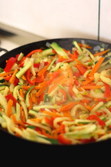Stir frying chopped leek, zucchinis, carrots and red bell peppers in a wok. Selective focus.
