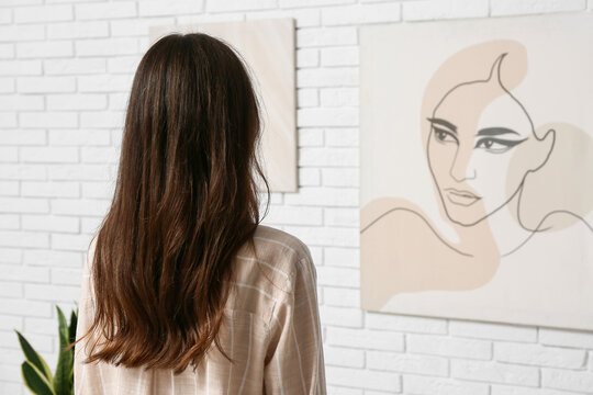 Young woman near paintings on white brick wall at art gallery exhibition, back view