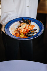 Waiter serving seafood pasta with mussels, cherry tomatoes, and parmesan in a gourmet restaurant