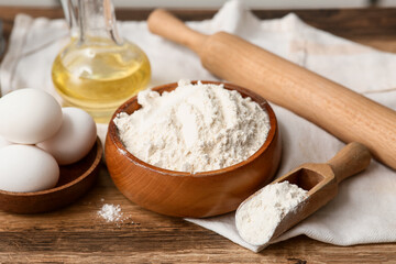 Bowl of flour with eggs, scoop, jug of oil and rolling pin for preparing dough on kitchen counter
