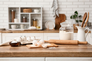 Flour in jar with eggs, rolling pin, salt and utensils for preparing dough on kitchen counter