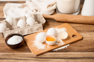 Board with eggs, flour, bowl of salt and rolling pin for preparing dough on wooden background