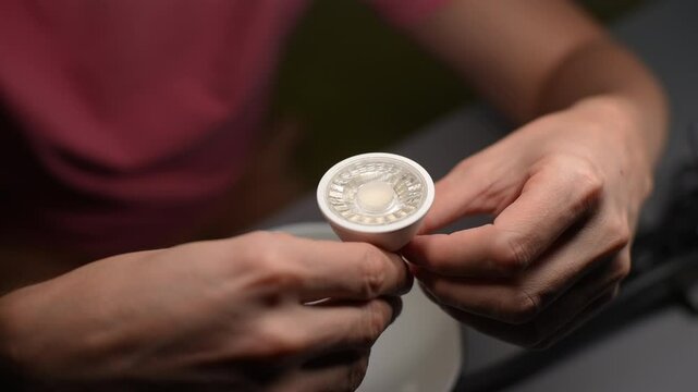 Professional electrician carefully checking gu10 led bulb into lamp socket. Concept of precise electrical maintenance and energy-saving technology upgrade, closeup, unrecognizable person, slow motion.