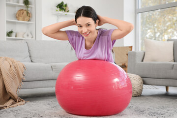Sporty young woman doing exercises on fitness ball at home