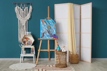 Interior of artist's workshop with painting on easel, folding screen and art supplies