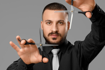 Handsome young bearded man with scissors on grey background