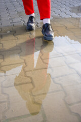 Striking pair of red pants and black shoes walking on a wet pavement, reflected in the water with geometric patterns.