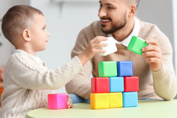 Happy father and his little son playing with colorful cubes at table in room