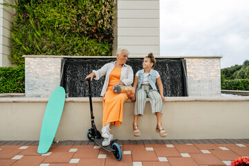 Happy grandmother and granddaughter push scooter on sunnyday