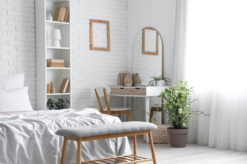 Interior of bedroom with dressing table, mirror and bed near white brick wall