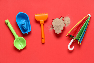 Beach toy mold, sand, decorative umbrella, toy ship, shovel and rake on red background