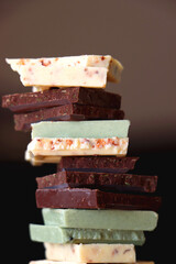Pile of various chocolate pieces on a plate. Dark, white and matcha chocolate. Selective focus.