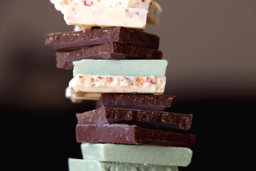Pile of various chocolate pieces on a plate. Dark, white and matcha chocolate. Selective focus.