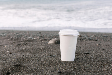two disposable white and black coffee cardboard cup against the backdrop of the sea coast, sandy seashore, pebble beach. mock up, place for logo