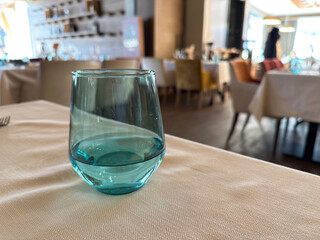 Soft focus shot of a turquoise glass tumbler on a restaurant table. Subtle lighting and blurred background create an elegant and minimalist composition. Copy space