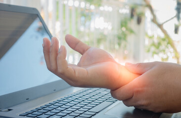 Young man working in a home office with carpal tunnel syndrome or wrist joint inflammation, massage on the hand and arm for relief pain from hard work for stiff, cramp symptom, carpal tunnel syndrome.