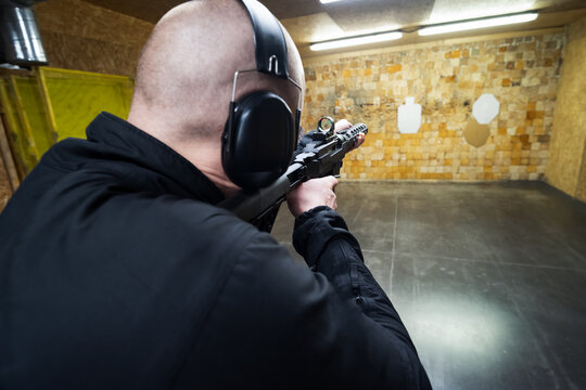 Bald man shoots a rifle at a shooting range, photo from the back.