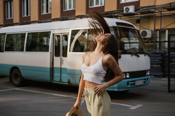 Young woman enjoying a sunny day posing in a fashionable outfit near a vintage bus, her hair flying in the wind