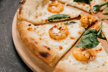 Close-up of gourmet seafood pizza slice with shrimp, melted cheese, and fresh spinach leaves