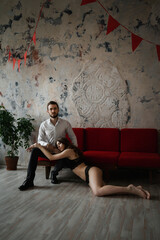 A girl in underwear lies at the feet of a guy in a business suit against the backdrop of a loft...