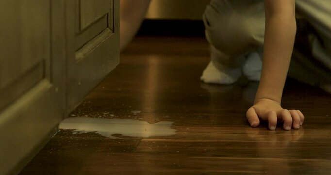 Small boy attempting to clean up milk spill on kitchen floor - close up