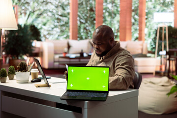 Self employed businessman works from home next to green screen on laptop, ensuring financial balance for his online startup. Entrepreneur freelancer telecommuting with mockup display.
