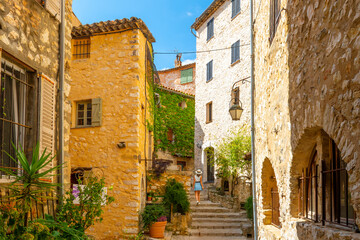 A woman walks up stairs surrounded by medieval stone buildings in the hilltop village of Tourrettes-sur-Loup, France, in the Alpes-Maritimes region of Southern France.	
