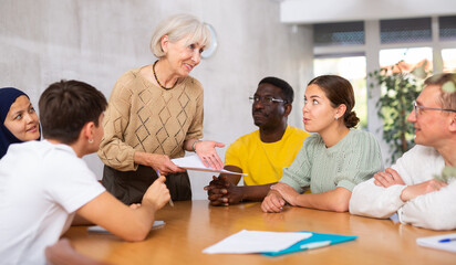 Obraz premium Elderly female manager holds round table meetings for employees of different nationalities