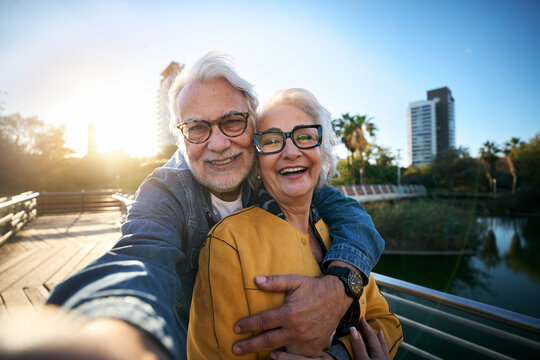 Portrait of happy senior couple taking selfie outdoors in a park of the city. Smiling elderly people traveling together on vacation. Cheerful man and woman posing for photo with mobile phone.