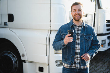 The truck driver drinks coffee. The truck driver rests in the parking lot after work