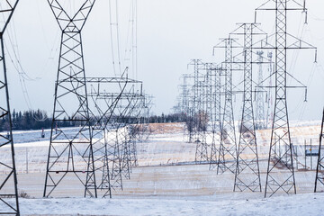 Power pole rows with electrical lines supplying energy to the power grid overlooking winter prairie fields in Rocky View County Alberta Canada.