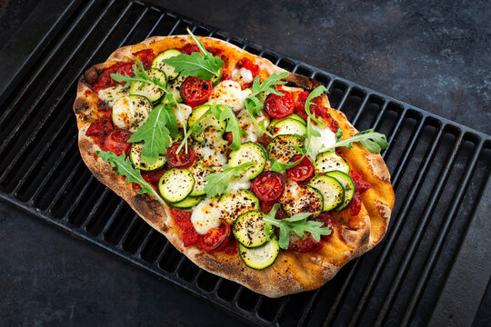 Traditional Italian pinsa bread prosciutto e salsa di pomodoro with tomatoes and zucchini in tomato sauce served as close-up on a rustic cast iron grillage