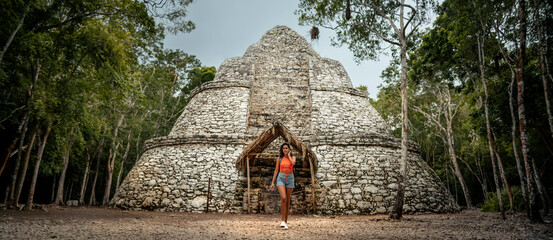 Toma panorámica de una mujer latina, viajera caminando frente a una pirámide/ruinas de la zona...