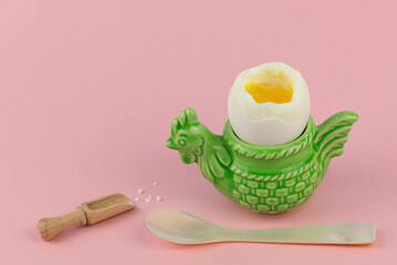 Das perfekt weich gekochte Ei in einem lustigen Eierbecher in Tierform (Huhn) mit Salz und Eierlöffel auf einem rosafarbenen flachen Hintergrund für Freude und Spaß beim frühstücken, Platz für Text © Uwe