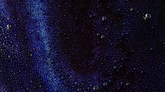 Close-up of dark, viscous liquid covered in tiny bubbles slowly flowing downwards. Creates mesmerizing patterns resembling cosmic landscapes or abstract paintings. Ideal for backgrounds, intros, music