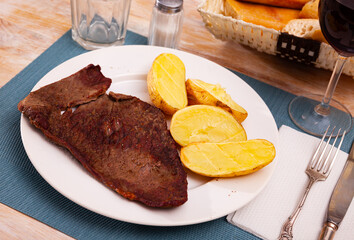 Fried barbecue beef meat with baked potato on a plate in a restaurant