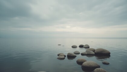A serene shoreline features smooth, rounded stones emerging from calm waters under a soft, overcast sky. The image evokes a sense of peace and introspection, inviting viewers to connect with natures